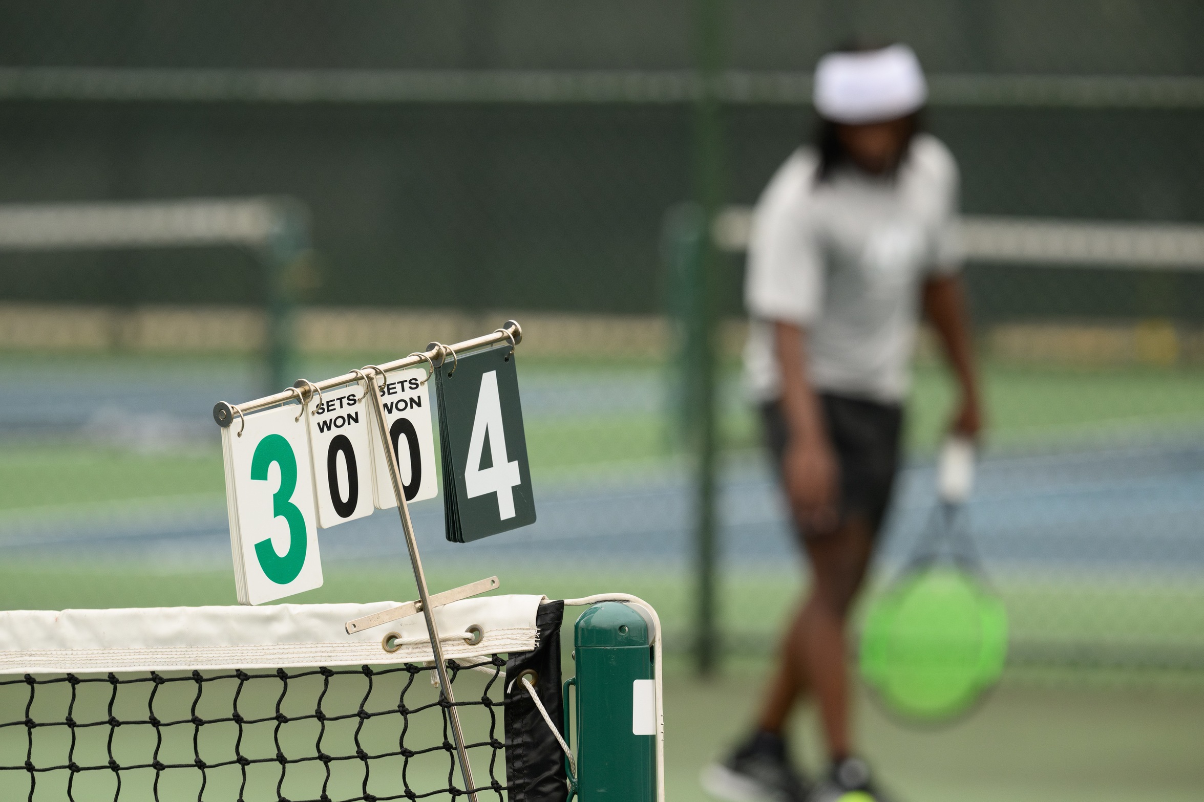 A Moraine Valley tennis player gets ready to serve the ball in the distance.